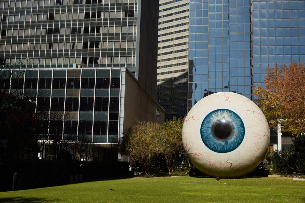 A giant Eye ball sculpture in the middle of downtown Dallas with an empty champagne bottle lying in the grass